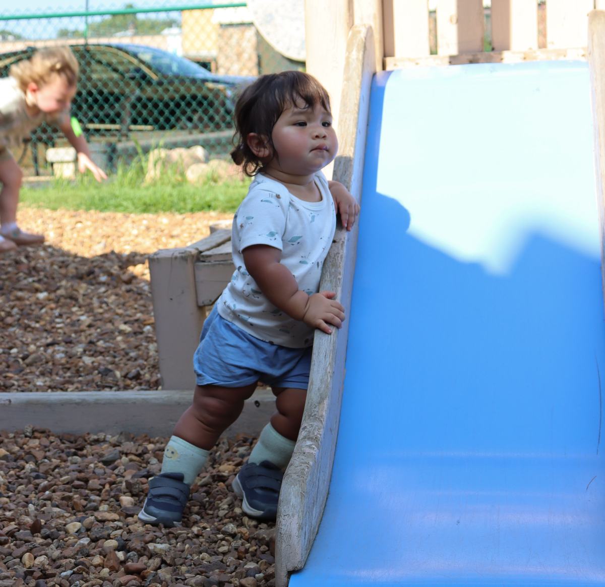 A toddler exploring the outdoor play area beside a blue slide