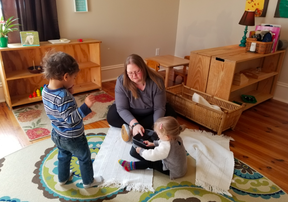 Ms. Lacey sitting on a rug working with two toddlers